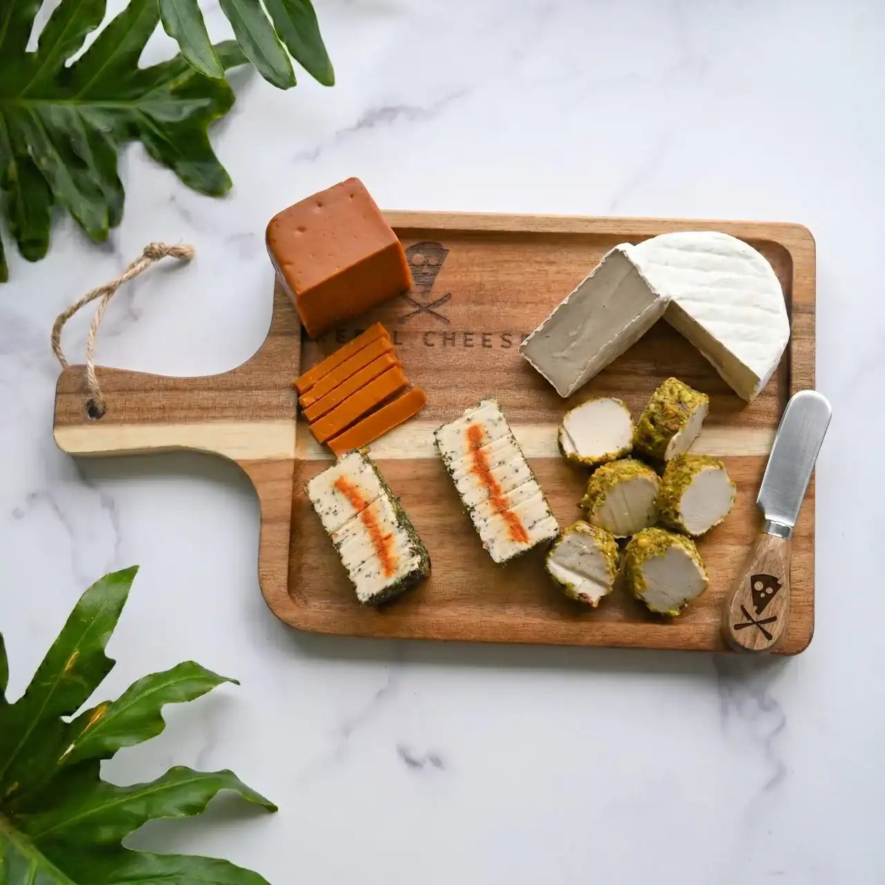 various dairy-free cheeses on a wooden cheese board and cheese knife on a white marble background