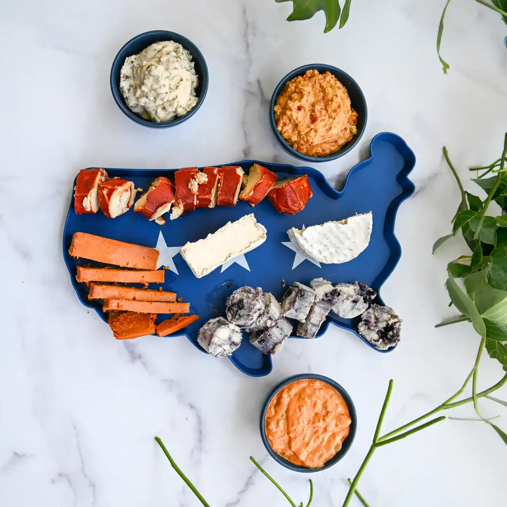 Blue platter shaped like the United States with various dairy-free cheeses on a marble surface