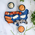 Blue platter shaped like the United States with various dairy-free cheeses on a marble surface