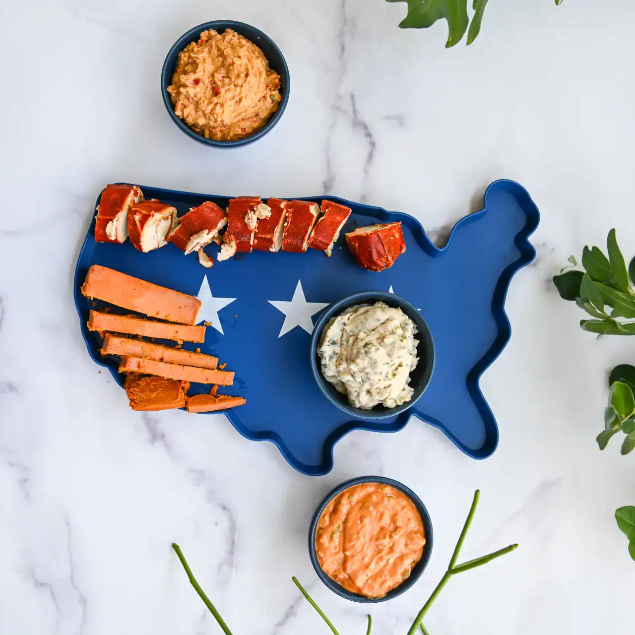 Blue USA-shaped platter with dairy-free cheeses on a marble surface