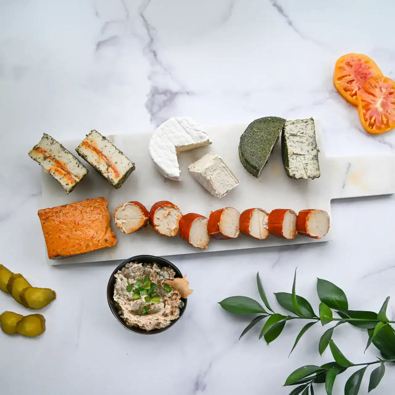 Assorted dairy-free cheese and charcuterie platter on a marble surface with a small bowl of Bacon Scallion Dip.