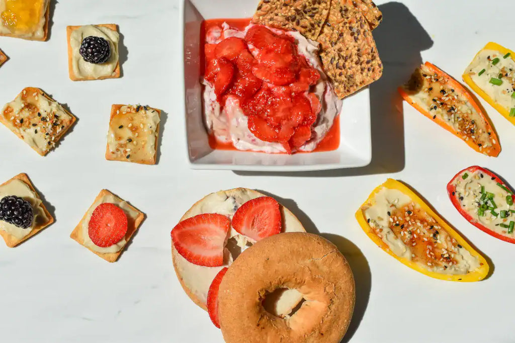 Assorted food items including bagels, fruit, and cream cheese on a white surface