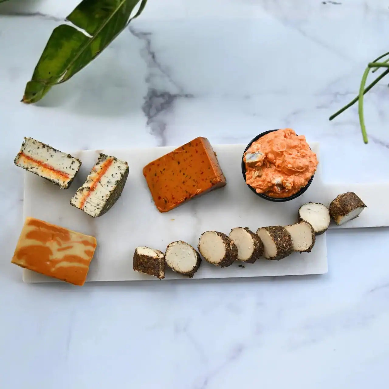 Assorted dairy-free cheeses on a marble surface with green leaves.