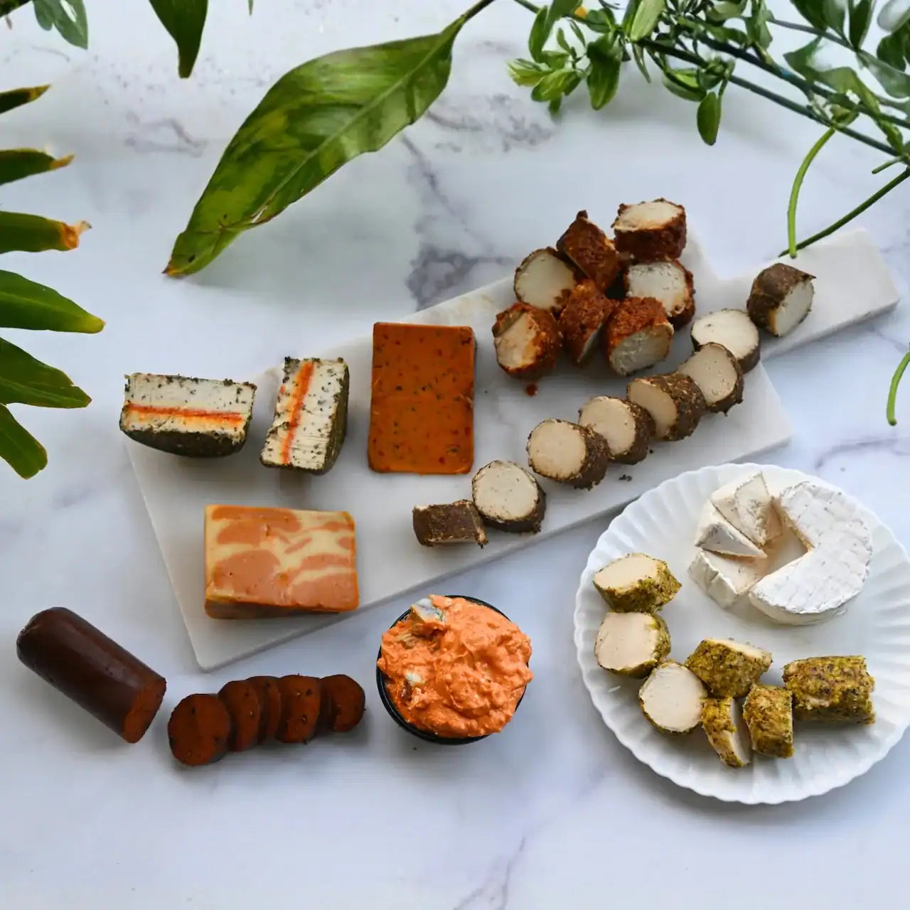 assorted dairy-free cheeses and vegan salami on a cheese board on a marble background