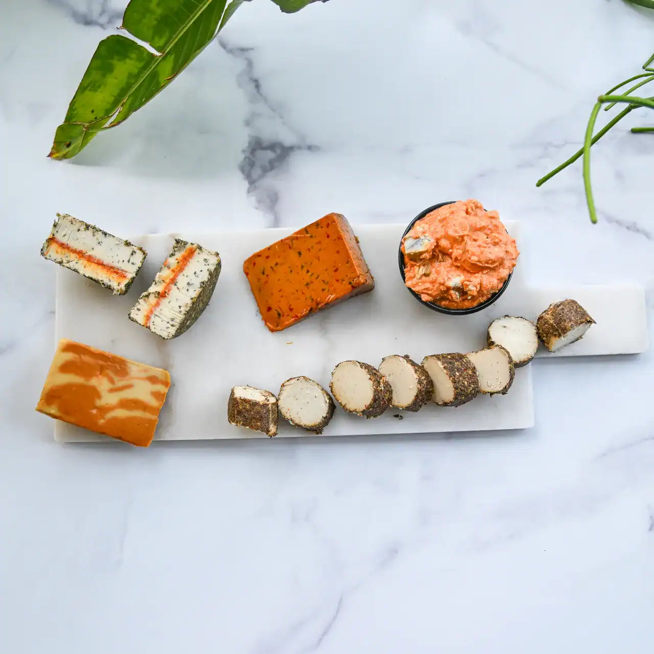 Assorted dairy-free cheeses on a marble surface with green leaves.