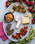 Platter of assorted cheeses and dips with flowers and pink napkins on a white surface