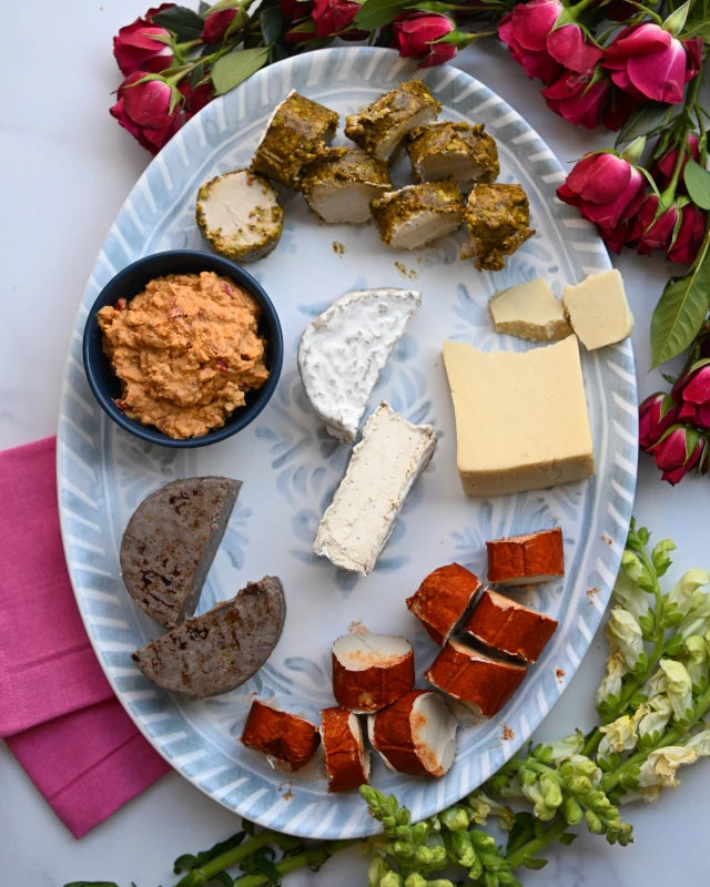 Platter of assorted cheeses and dips with flowers and pink napkins on a white surface