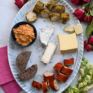Platter of assorted cheeses and dips with flowers and pink napkins on a white surface
