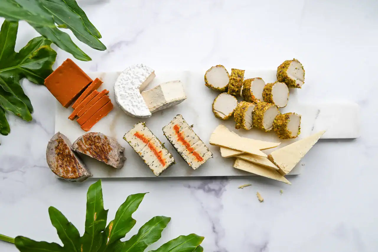 Assorted dairy-free cheese slices on a marble surface with green leaves.