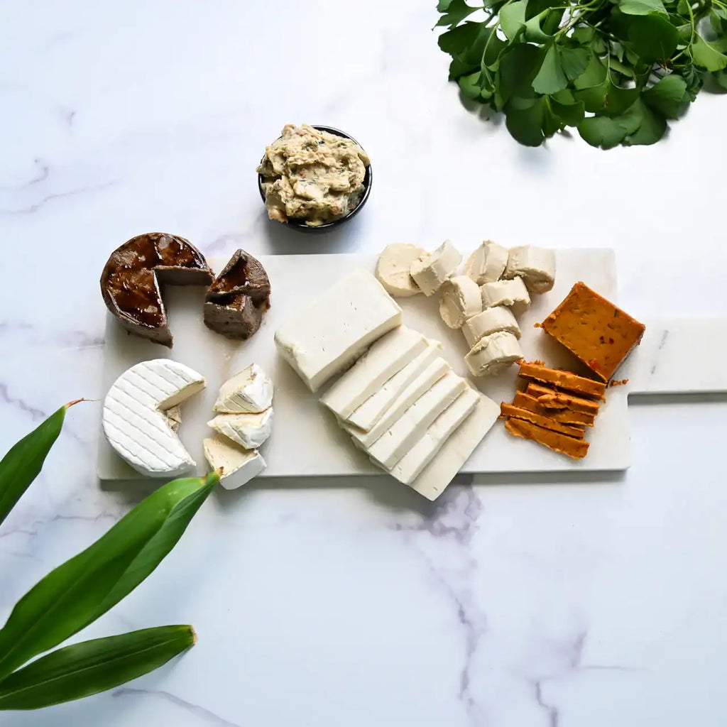 six dairy free cheeses on a marble board on a white background