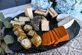 Assorted cheeses on a black plate with decorative flowers in the background