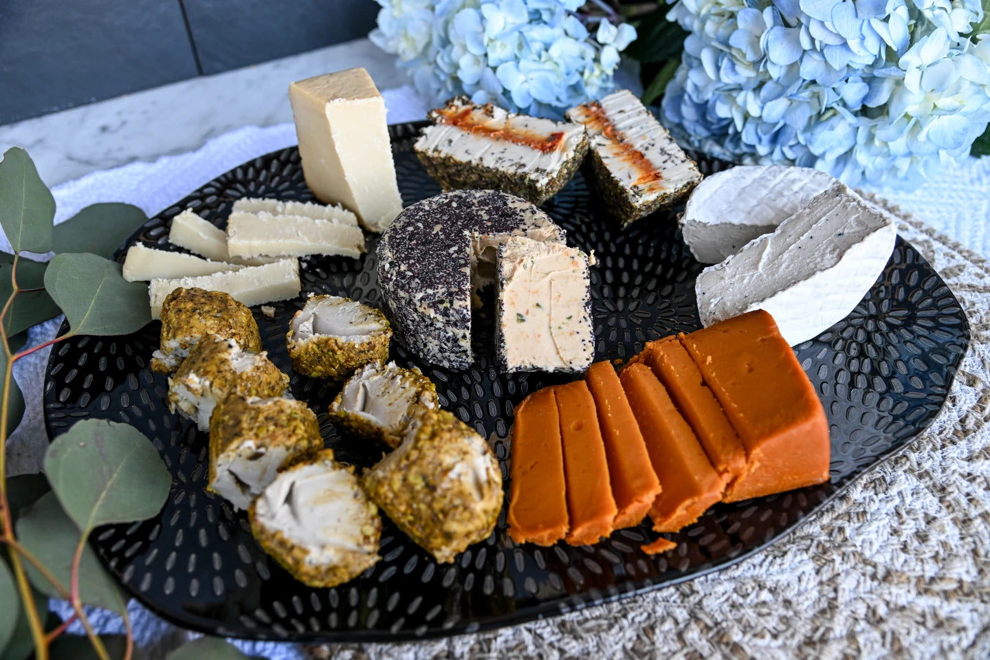 Assorted cheeses on a black plate with decorative flowers in the background