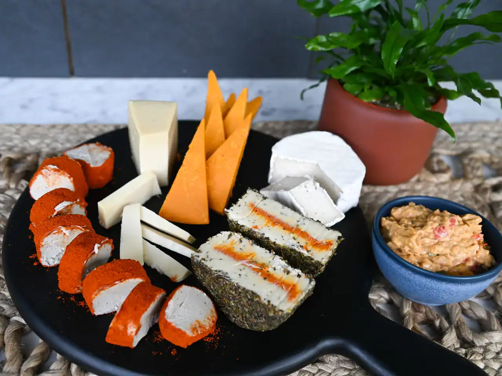 Assorted dairy-free cheeses sliced on a black cheese board, and a bowl of pimento cheese on the side.