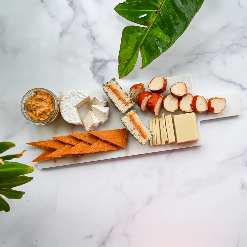 assorted dairy-free cheeses sliced on a white marble cheese board and a small mason jar of Pimento Cheese from Rebel Cheese.