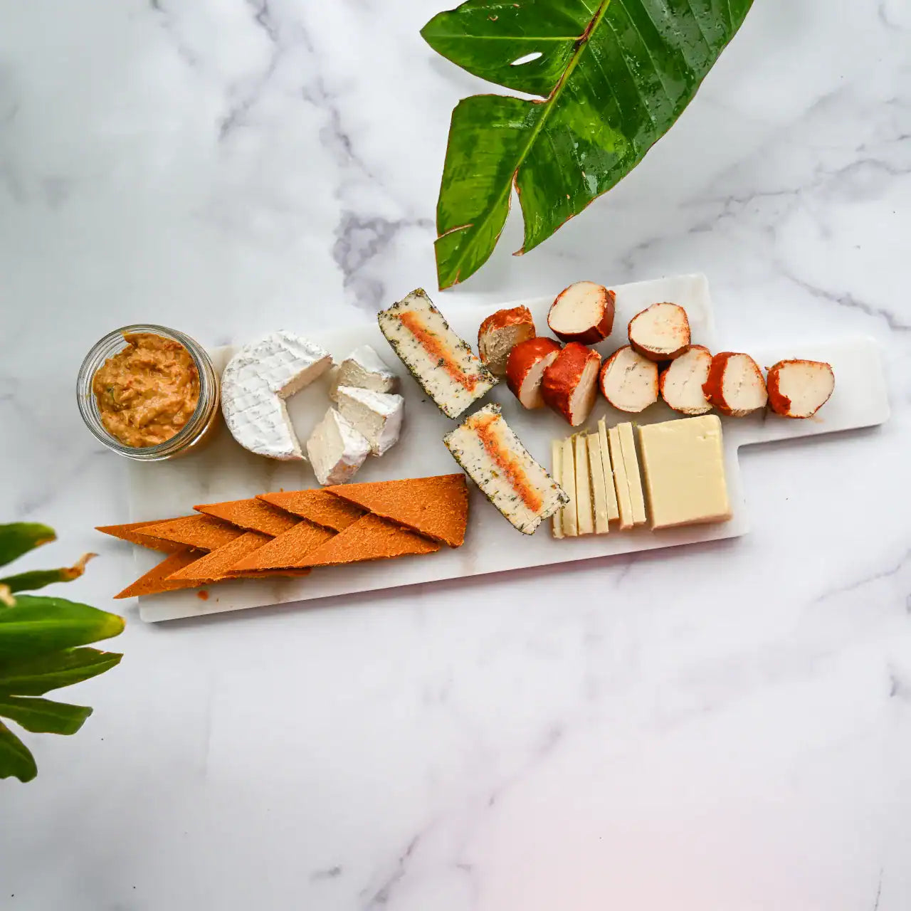 assorted dairy-free cheeses sliced on a white marble cheese board and a small mason jar of Pimento Cheese from Rebel Cheese.