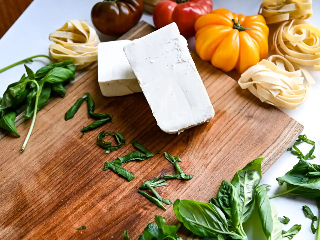 dairy-free mozzarella on a wooden cutting board with pasta and heirloom tomatoes in the background