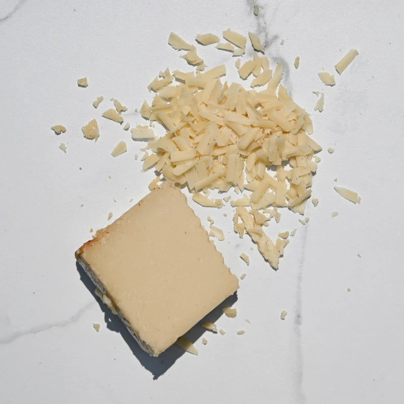 Block of Parmesan cheese with grated cheese on a white marble surface