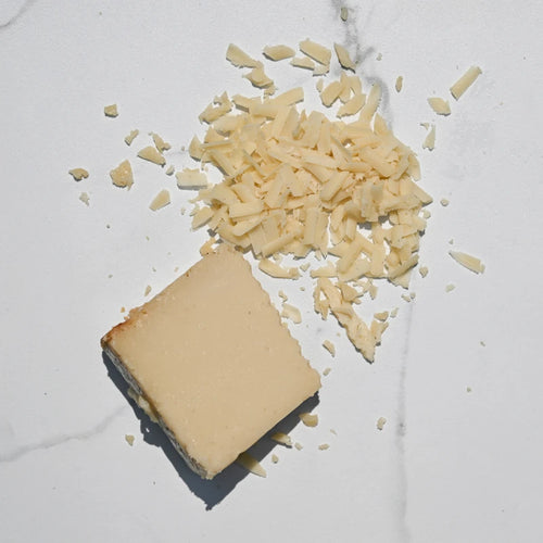 Block of Parmesan cheese with grated cheese on a white marble surface