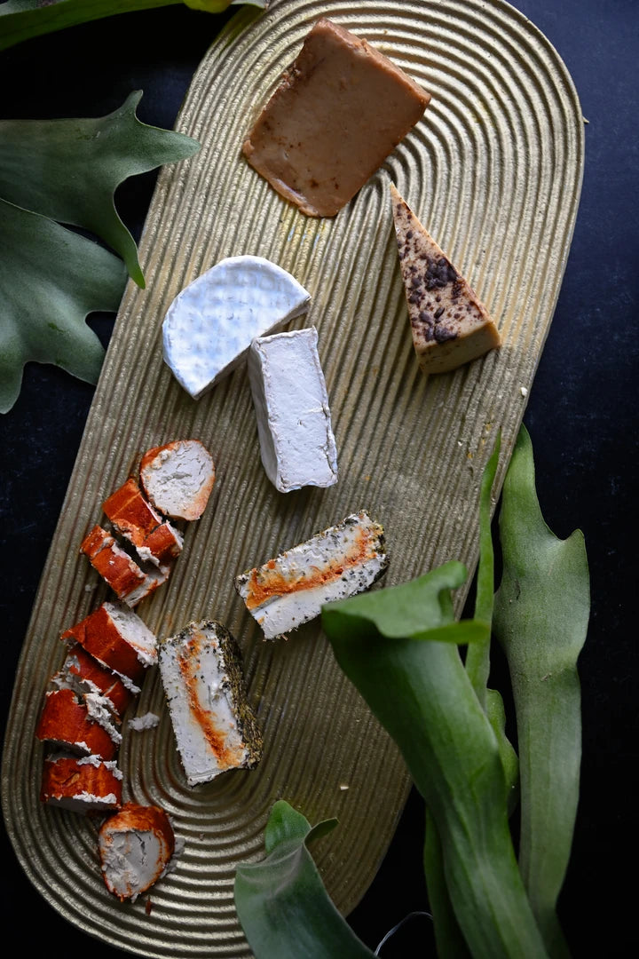 Assorted vegan cheeses on a wooden board with green leaves in the background
