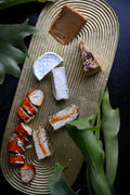 Assorted vegan cheeses on a wooden board with green leaves in the background