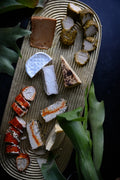 Assorted vegan cheeses on a wooden board with greenery around