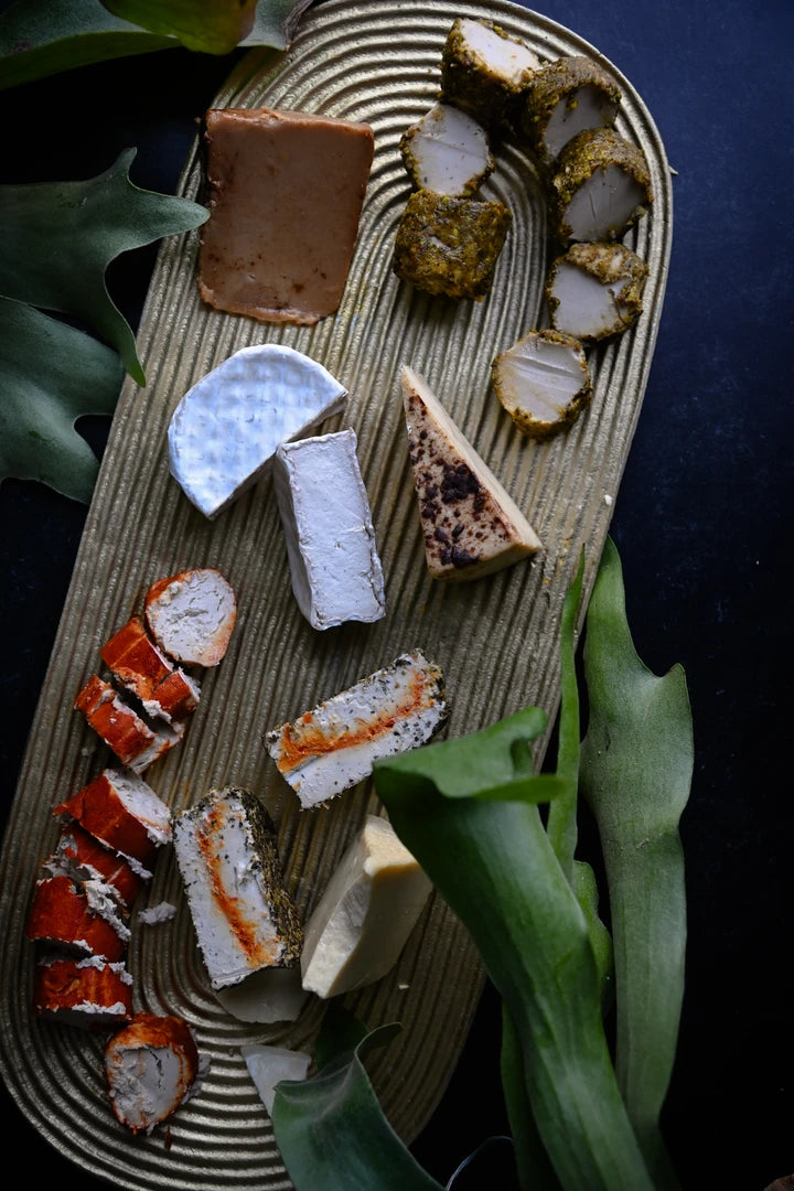 Assorted vegan cheeses on a wooden board with greenery around