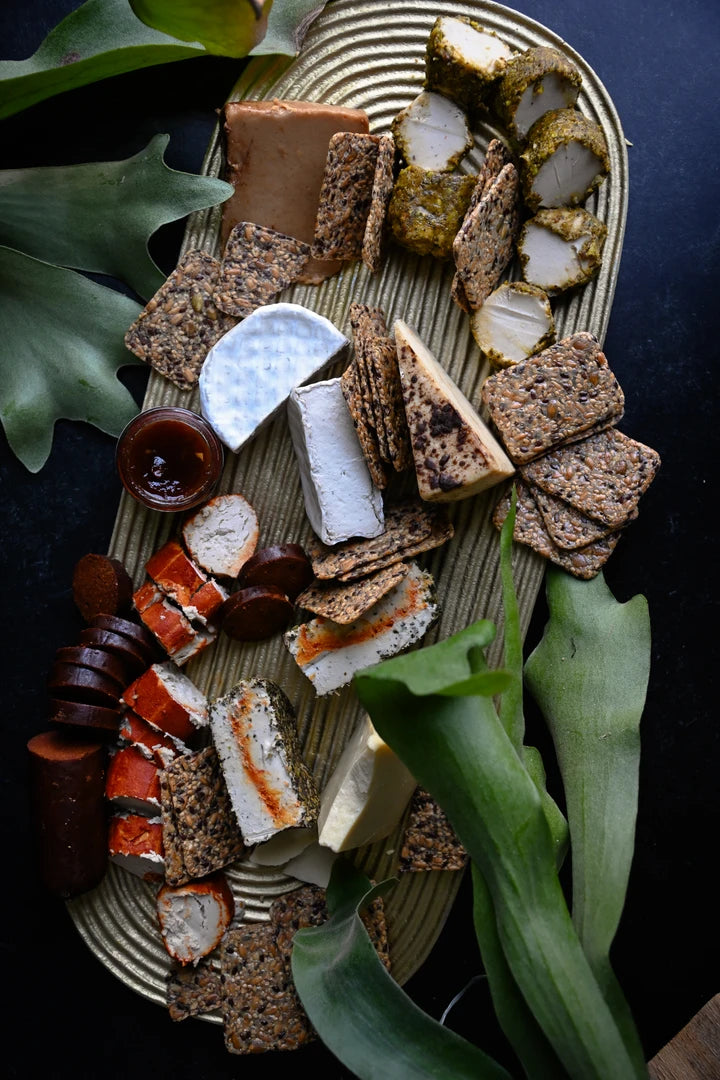 Assorted crackers, cheese, and vegan salami on a decorative platter with greenery.