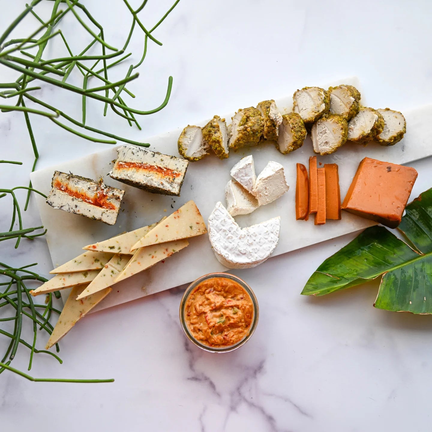 Assorted dairy-free cheeses on a marble cheese board on a white background.