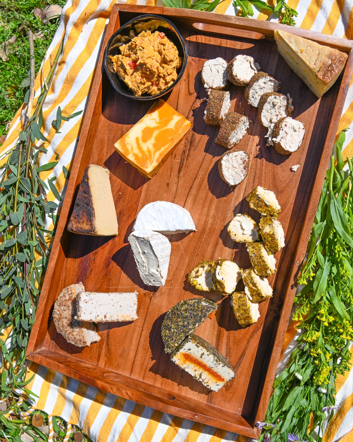 Wooden cheese board with various types of cheese on a striped fabric background.