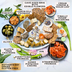 Assorted food items including brie, crackers, olives, and other snacks on a white surface with labels.