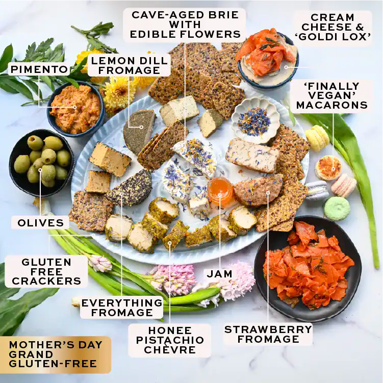 Assorted food items including brie, crackers, olives, and other snacks on a white surface with labels.