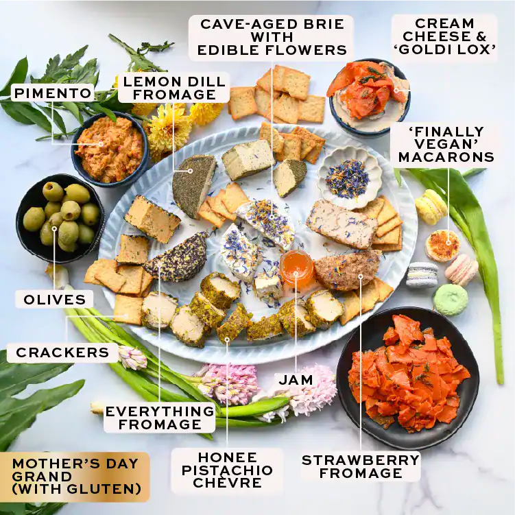Assorted food items including brie, crackers, olives, and other snacks on a white surface with labels.
